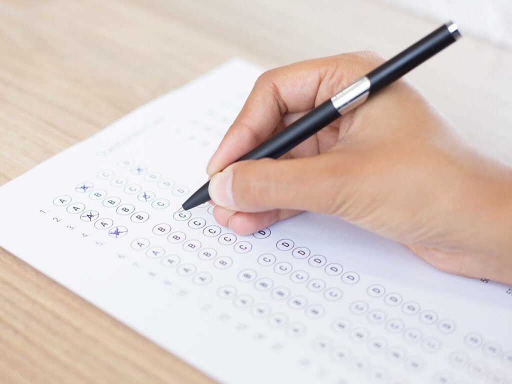 Closeup of hand holding pen and filling out questionary form on table