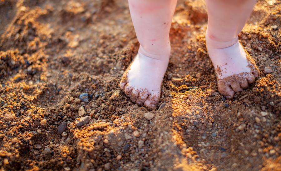 Children's bare feet in summer on a golden sandy beach close-up. Children's bare feet in summer on a golden sandy beach close-up. The concept of child safety. The concept of recreation with children.