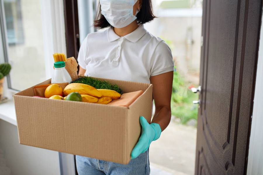 Volunteer woman in white protective mask and gloves delivery donation box at home Volunteer woman in white protective mask and gloves delivery donation box at home, Courier with packing box with food, contactless delivery, Service quarantine pandemic coronavirus.