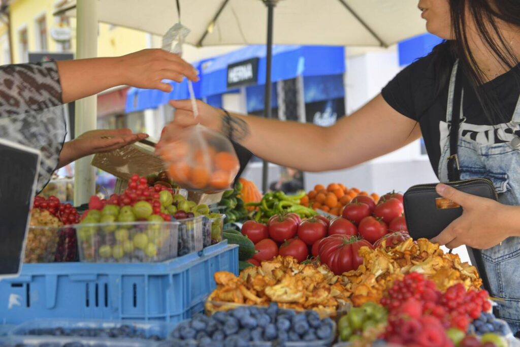 Young girl buying fruits and vegetables at farmers market. Sustainable lifestyle. Fresh organic produce for sale at local farmers market.