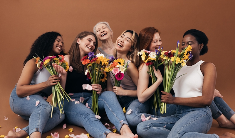 Six women of different ages and body types holding bouquets while sitting in studio against a brown background Six women of different ages and body types holding bouquets while sitting in studio against a brown background