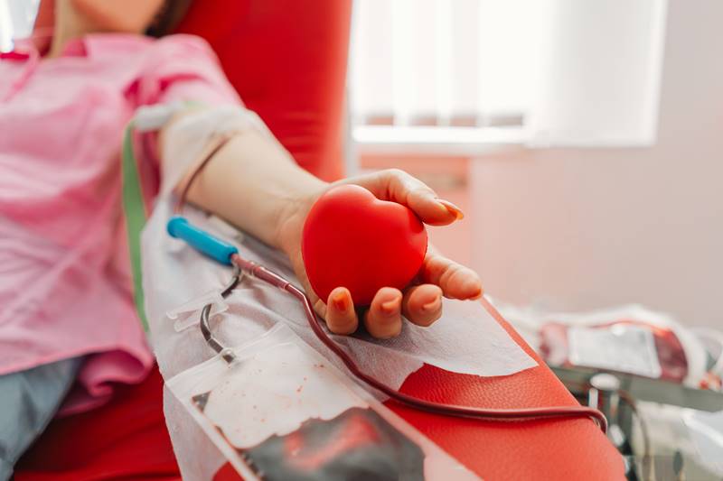 Young woman making blood donation in hospital. Blood donation. Young woman making blood donation in hospital. A woman donates blood while holding a red heart. Blood donation.