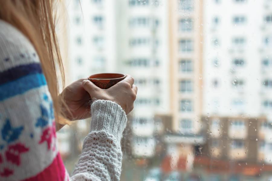 A girl with a mug in her hands at the window. Morning coffee on a rainy day. The concept of autumn sadness, cold and not cozy mood. It's raining outside. Warm house romance comfort. Copy space