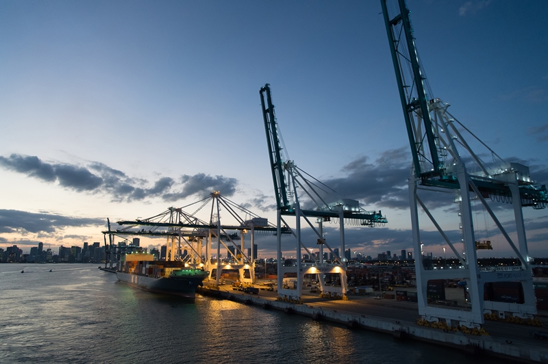 Miami, USA - March 01, 2016: freight carrier and cranes on evening sky. Cargo carrier on pier side. City skyline at dusk. Shipping and shipment. Cargo loading.