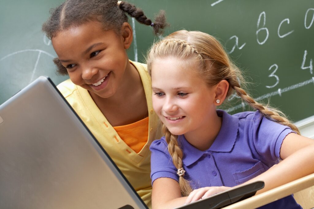 Portrait of two schoolgirls looking at the laptop during lesson