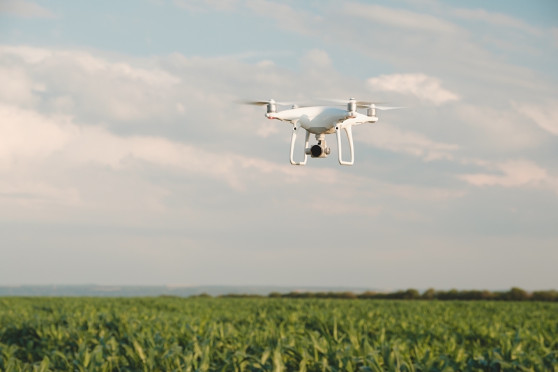 White drone hovering in a bright blue sky. Drone copter flying with digital camera