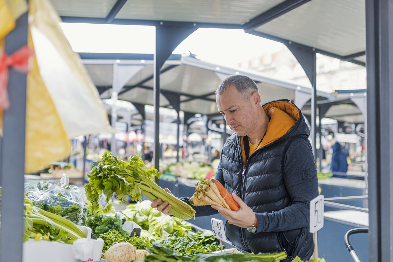Mature man picking vegetables at farmers's market. Man buying organic fruits and vegetables at an open street market. Local Farmers Market. Fresh produce: vegetables