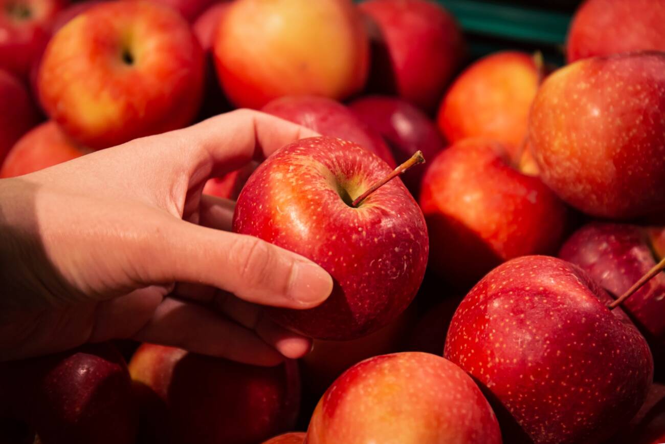 Close-up, an apple in a woman's hand, a selection of fruits in a supermarket.
