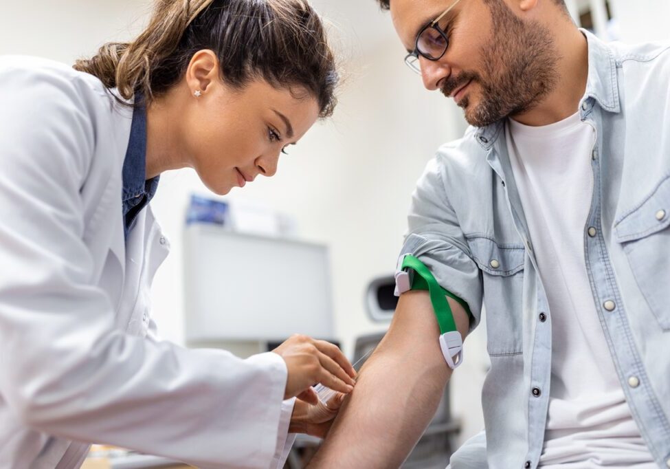 Friendly hospital phlebotomist collecting blood sample from patient in lab. Preparation for blood test by female doctor medical uniform on the table in white bright room