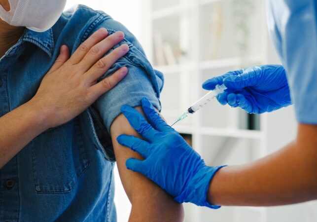 Young Asia lady nurse giving Covid-19 or flu antivirus vaccine shot to senior male patient wear face mask protection from virus disease at health clinic or hospital office. Vaccination concept.