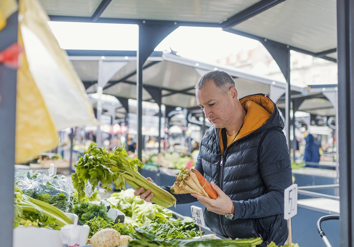 Mature man picking vegetables at farmers's market. Man buying organic fruits and vegetables at an open street market. Local Farmers Market. Fresh produce: vegetables