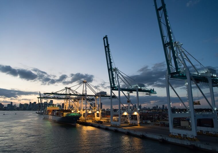 Miami, USA - March 01, 2016: freight carrier and cranes on evening sky. Cargo carrier on pier side. City skyline at dusk. Shipping and shipment. Cargo loading.