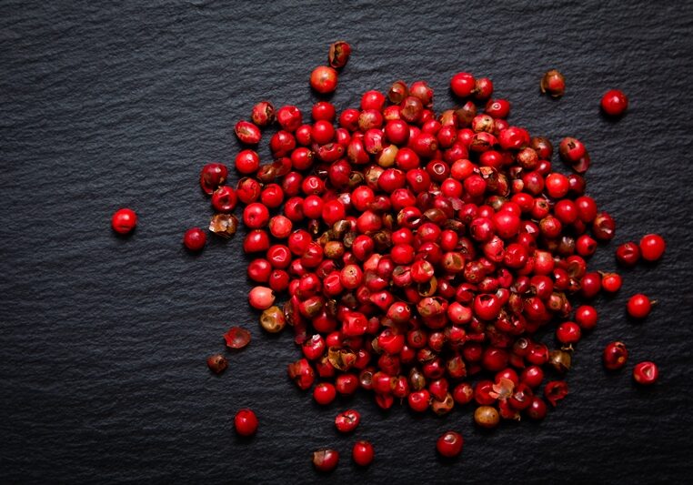 Organic peppercorn or pink pepper in iron scoop on black slate stone background