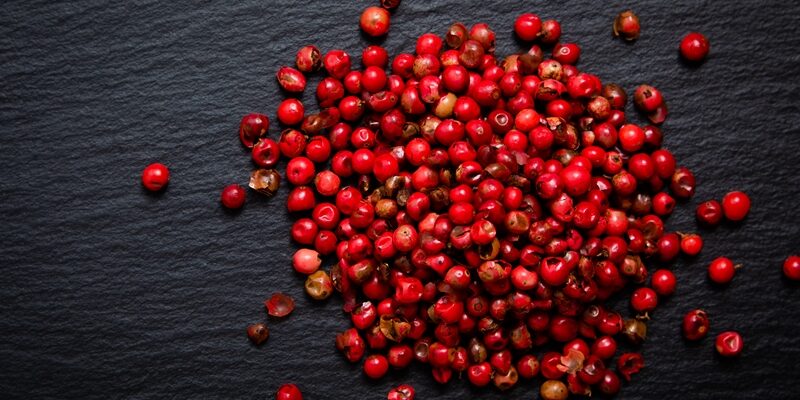 Organic peppercorn or pink pepper in iron scoop on black slate stone background