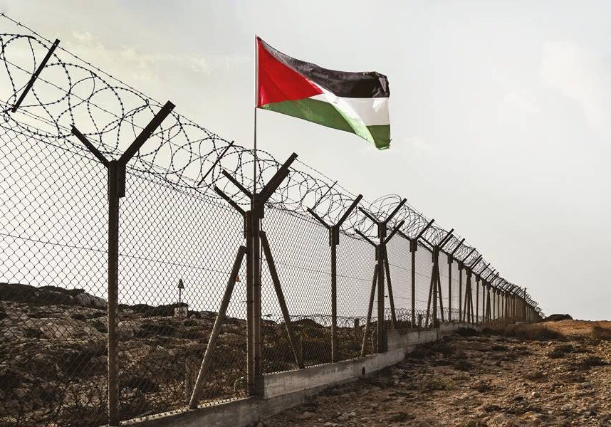 View of palestinian flag behind barbed wire in the desert against cloudy sky.