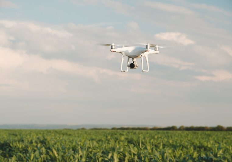White drone hovering in a bright blue sky. Drone copter flying with digital camera