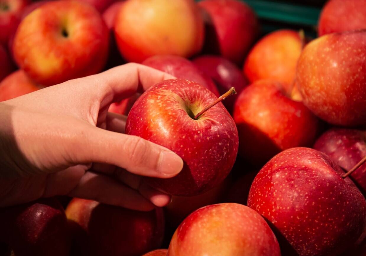 Close-up, an apple in a woman's hand, a selection of fruits in a supermarket.